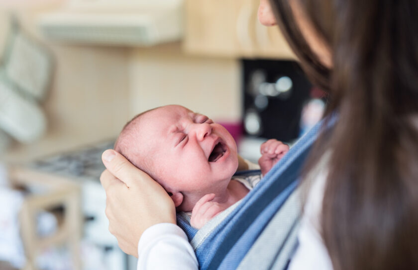 Unrecognizable young mother with her crying son in sling